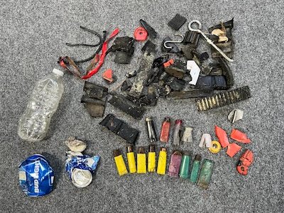 This photo contains a large number of items found along the road including: plastic water bottle, crushed beer can, various rubber and plastic parts from snowmobiles, about 18 bullet casings and other miscellaneous paper and plastic products.